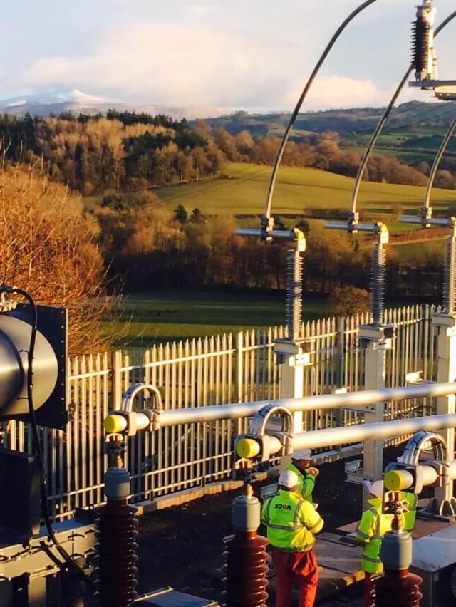 Rock Power Connection employees in high vis clothing, working on an electrical connection with the British countryside in the background